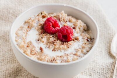 A bowl of thick, creamy keto oatmeal made with riced cauliflower and topped with red raspberries.