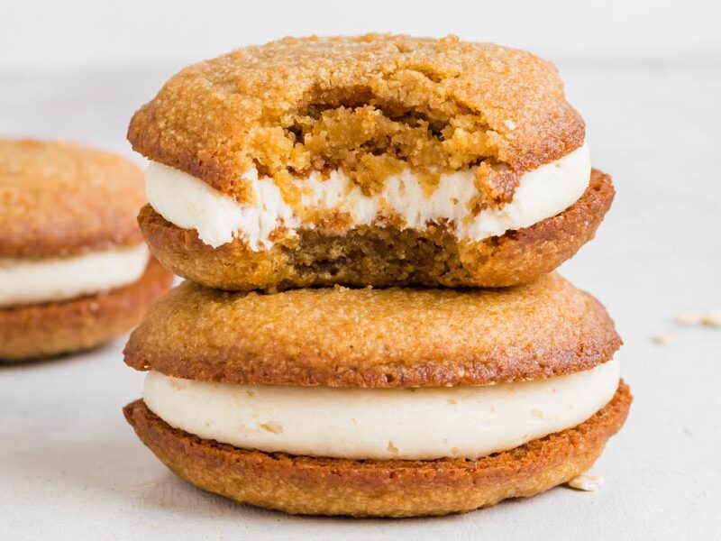 A stack of two oatmeal cream pies. The top pie has a bite taken out of it.