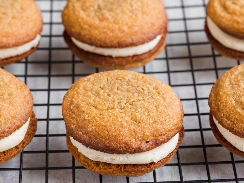 Oatmeal cookies filled with cream filling on a wire rack lined in rows.