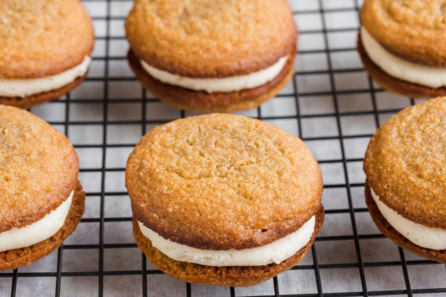 Oatmeal cookies filled with cream filling on a wire rack lined in rows.