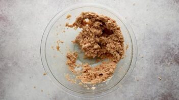 A clear glass bowl with wet cookie ingredients inside.