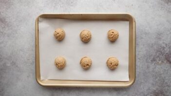A baking tray with six cookie dough balls scooped on the tray.