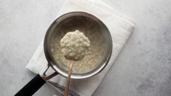 A spoon holding a bite of thick oatmeal over a saucepan.