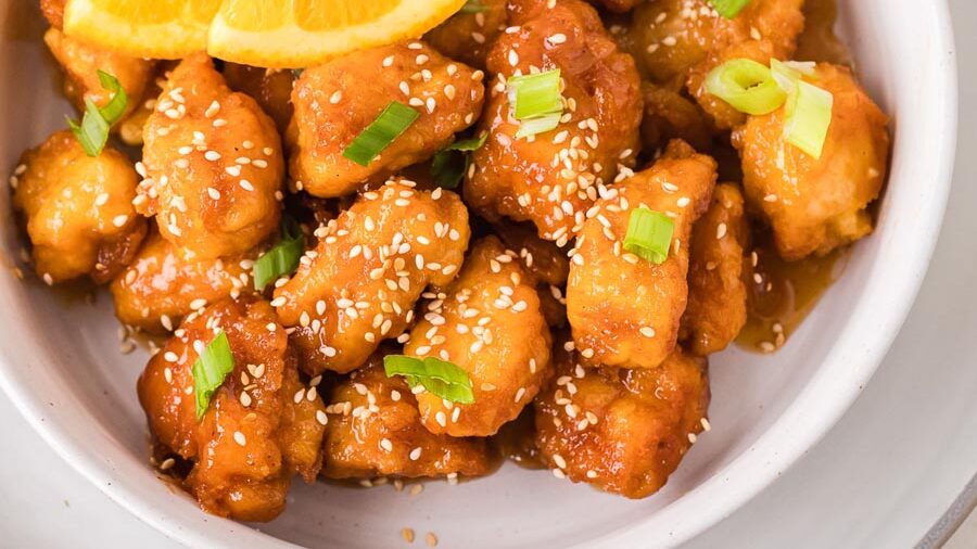 Keto orange chicken coated in a glossy orange sauce and topped with sesame seeds, green onions, and fresh orange slices.