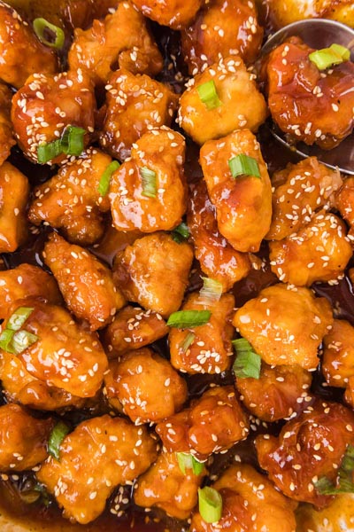 Overhead close-up of crispy keto orange chicken tossed in orange sauce and garnished with sesame seeds and green onions.