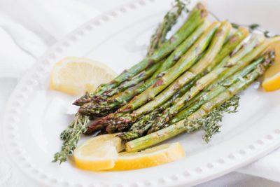 crispy keto asparagus on a white platter with lemon slices and thyme sprinkled around