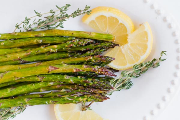 crisp oven baked asparagus on a white serving platter with lemon slices and thyme
