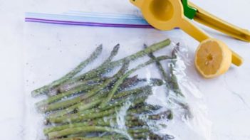 asparagus spears seasoned in a ziploc bag with a juicer and lemons nearby