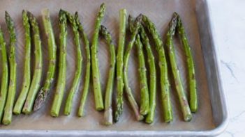 unbaked asparagus spears lined up on a parchment lined baking tray