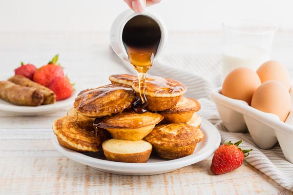 pouring maple syrup over a stack of mini pancakes shaped like pies