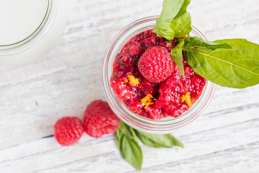 red raspberries and basil leaves with orange zest on top of a jar