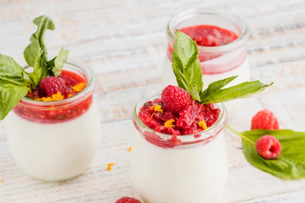 three panna cottas in jars with berries and basil