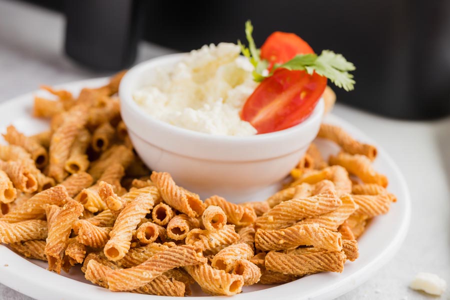 a plate with baked pasta chips on it next to a bowl of dip