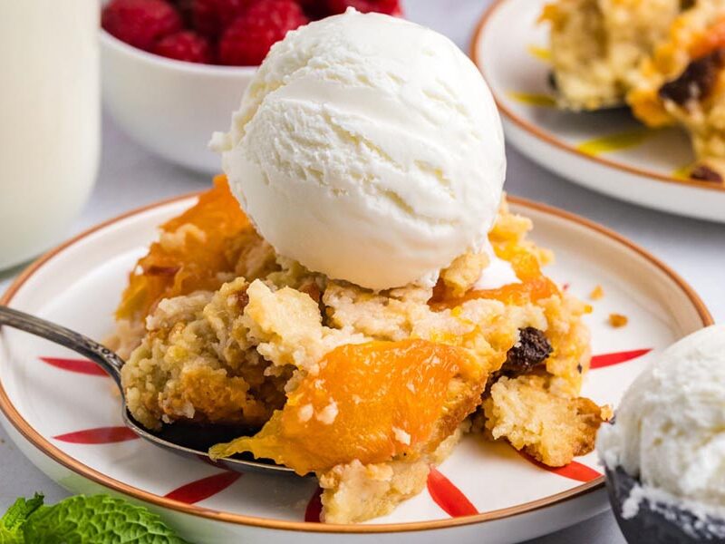 Warm, gooey peach cobbler on a plate topped with creamy ice cream.