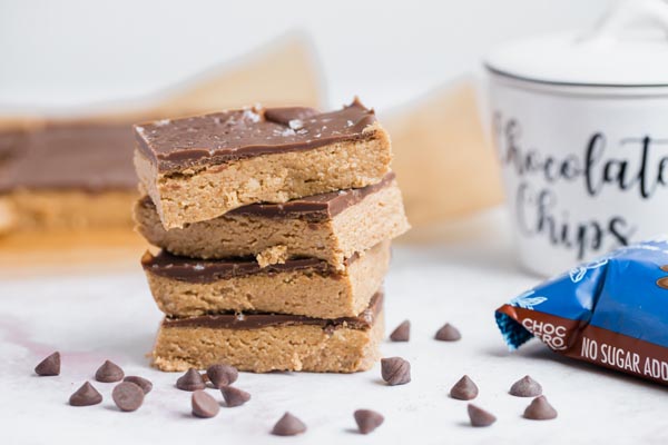 four chocolate peanut butter bars with chocolate chips in a container and around