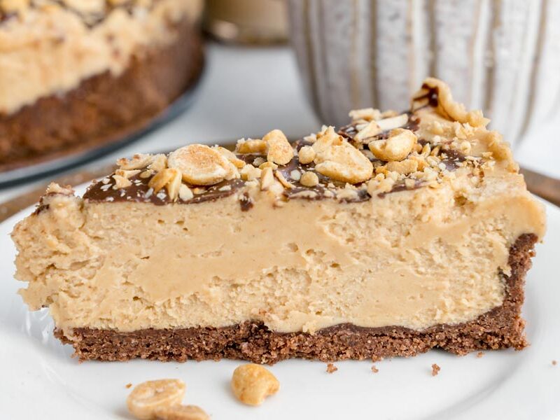 Close-up of a creamy keto peanut butter cheesecake slice with a chocolate crust and peanut topping.