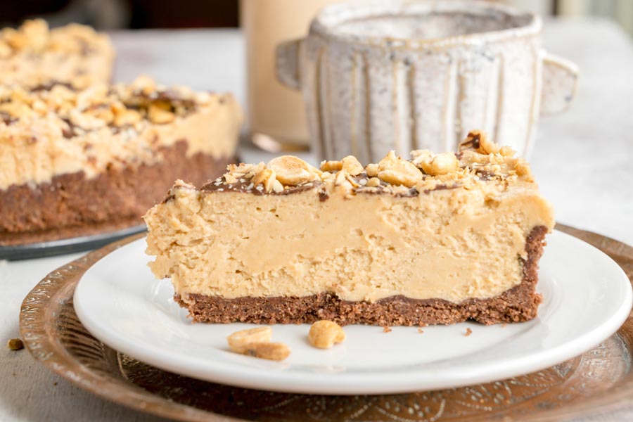 Side view of a rich keto peanut butter cheesecake slice with a chocolate cookie crust and peanut topping.