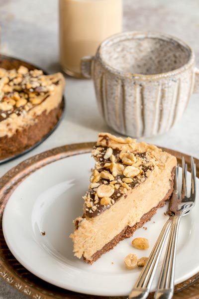 Slice of no-bake keto peanut butter cheesecake served with forks beside a whole cheesecake in the background.