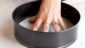 Hand pressing parchment paper into the bottom of a springform pan to prepare it for cheesecake.