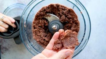 Chocolate crust mixture being blended in a food processor and pressed together by hand.