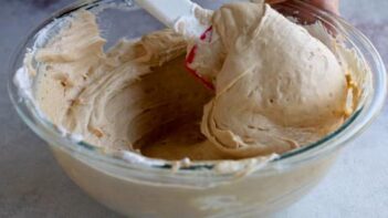 Creamy peanut butter cheesecake filling being folded together in a glass mixing bowl with a spatula.