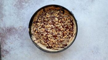 Keto peanut butter cheesecake topped with chocolate drizzle and chopped peanuts before chilling.