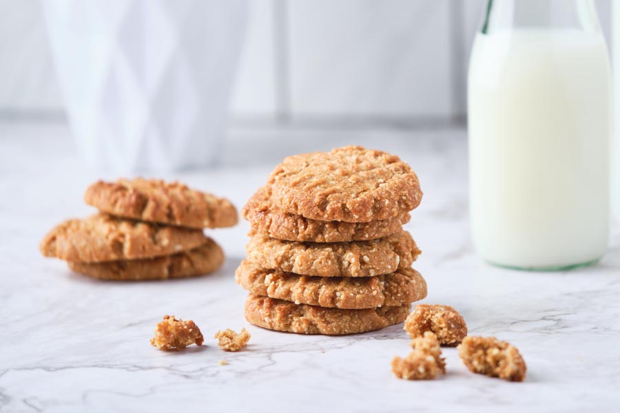 A stack of peanut butter cookies in from of another stack with a jug of milk behind them.