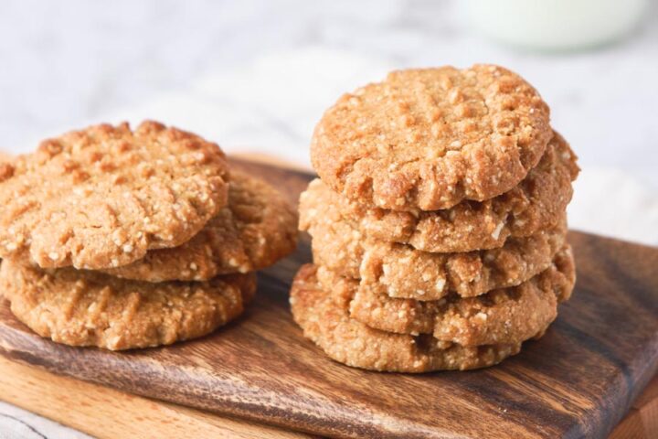 Close up of peanut butter cookies with a crisscross pattern in stacks on a cutting board.