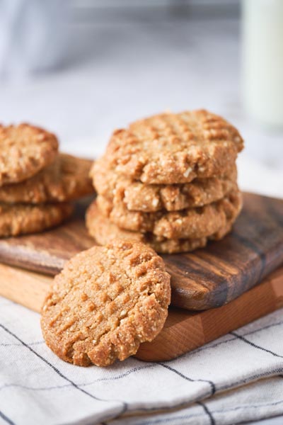 A stack of cookies on a cutting board with a cookie falling off the ball.
