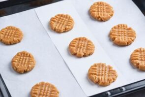 Unbaked cookies on a tray with parchment paper with crosshatched patterns.