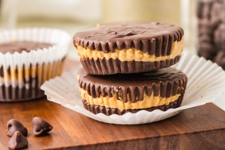 Stack of keto peanut butter cups with a thick peanut butter center and chocolate coating on a wooden board.