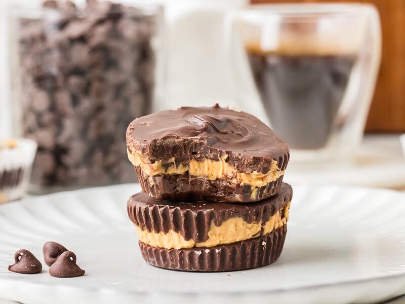 Two keto peanut butter cups stacked with a bite taken out, showing the creamy peanut butter filling.
