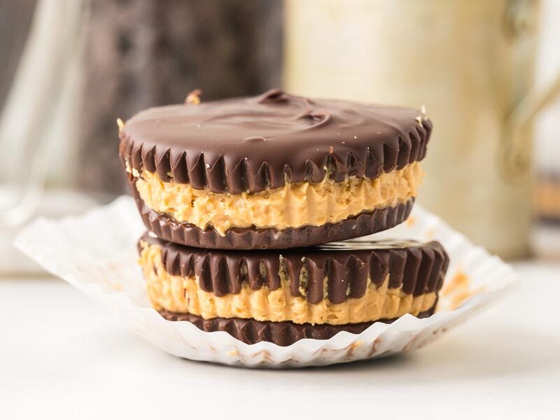 Close-up of two keto peanut butter cups stacked in paper liners with a smooth chocolate top.