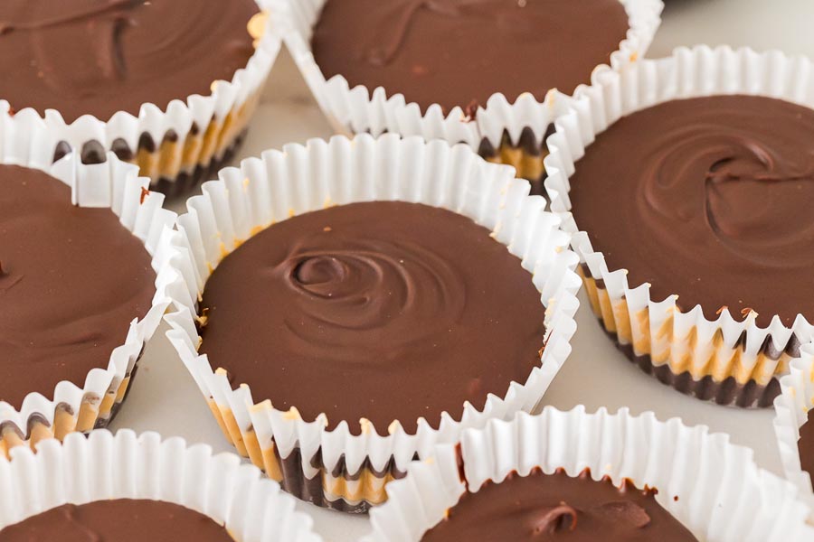Batch of homemade keto peanut butter cups in white liners with glossy chocolate tops.