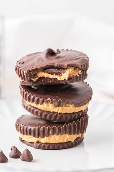 Stack of keto peanut butter cups with one partially bitten, revealing the layered chocolate and peanut butter center.
