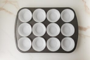 Muffin tin lined with white paper cupcake liners arranged in rows for making peanut butter cups.