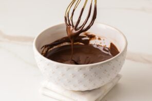 Bowl of melted chocolate with a whisk lifting glossy chocolate to show smooth consistency.