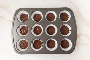 Muffin tin with 12 paper liners filled with melted chocolate.