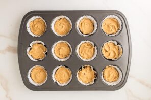 Muffin tin with peanut butter filling scooped evenly into each chocolate-lined cup.