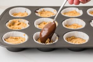 Spoon adding a final layer of melted chocolate over the peanut butter filling in each cup.