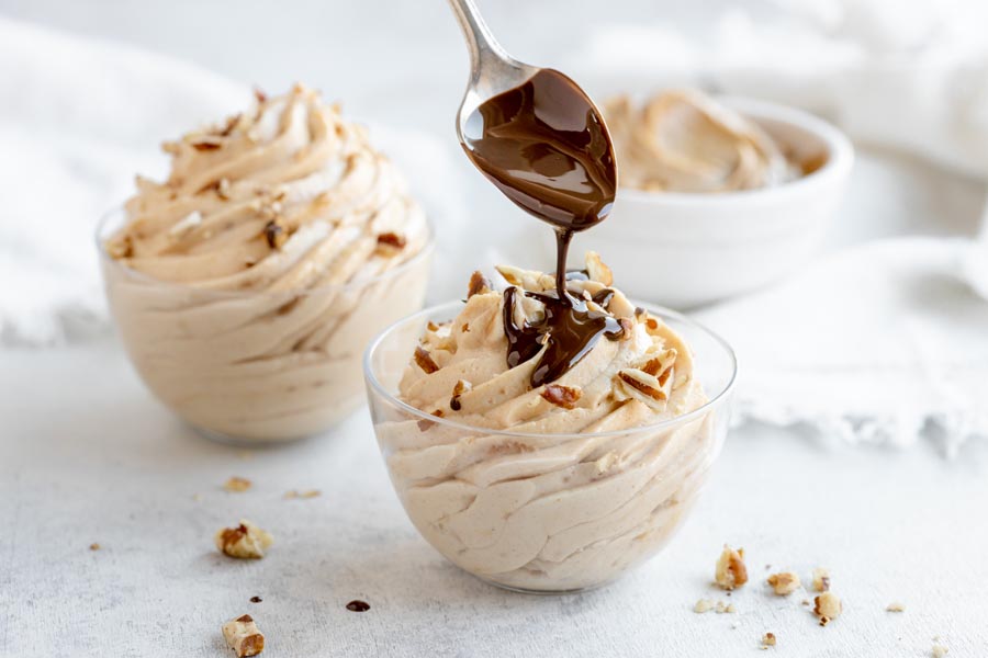 drizzling melted chocolate on top of a bowl of silky peanut butter mousse topped with nuts