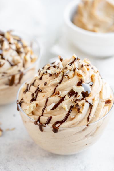 a swirly pile of peanut butter mousse in a small clear container topped with drizzled chocolate and nuts