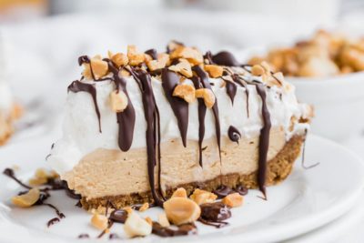 a slice of peanut butter cream pie on a white plate with chocolate and nuts on top