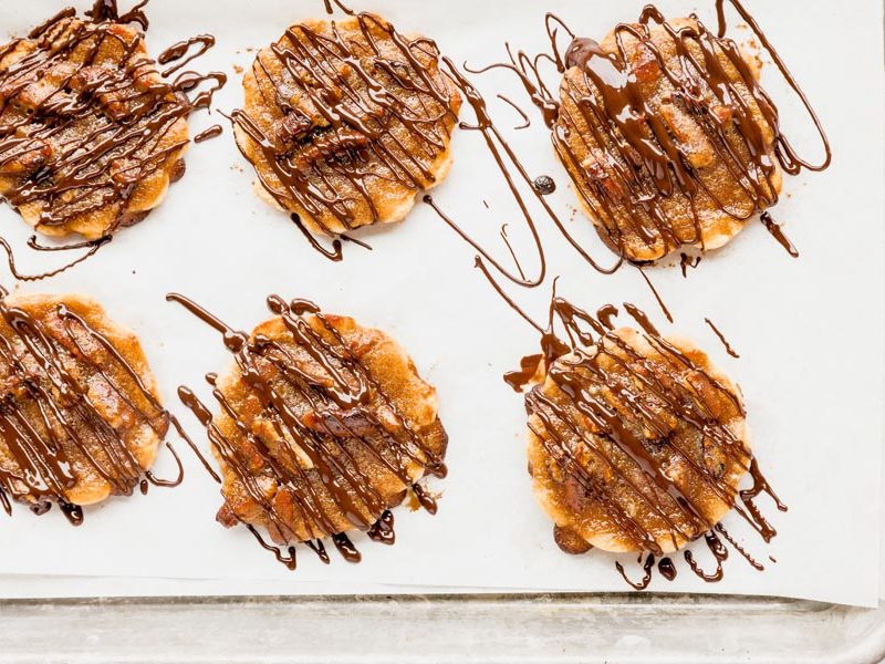 a baking tray with six pecan pie cookies on it drizzled with melted chocolate