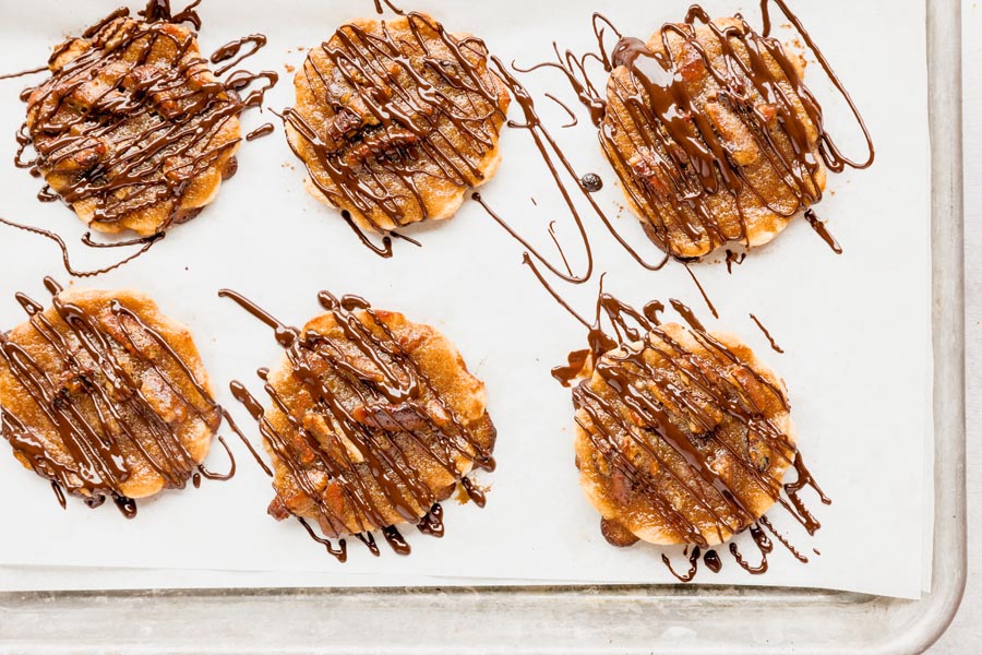 a baking tray with six pecan pie cookies on it drizzled with melted chocolate