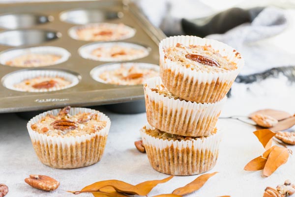 muffins stacked up next to leaves and a muffin pan in the background