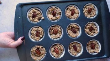 holding a muffin tin with muffin batter filled liners toped with a whole pecan