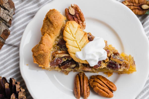 a slice of pecan pie on a plate with pecans scattered and a dollup of whippe cream