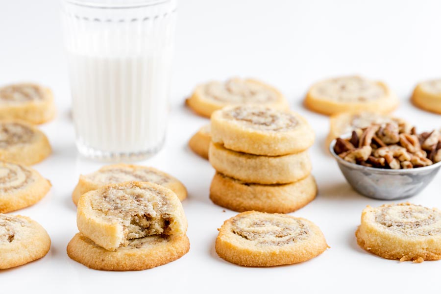 stacks of pinwheel cookies next to crushed pecans and a glass of milk
