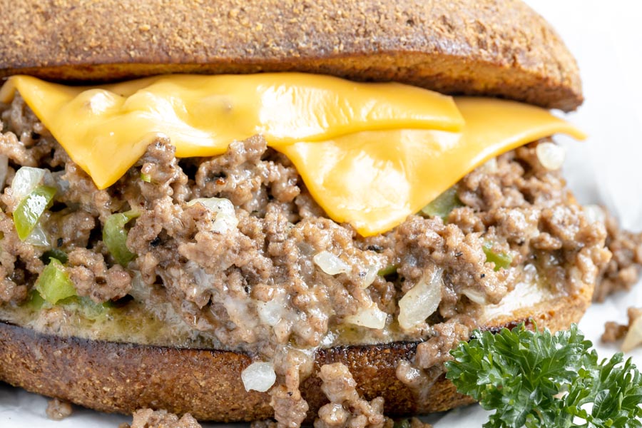 close up of melted american cheese on top of ground beef cheesesteak inside a bun